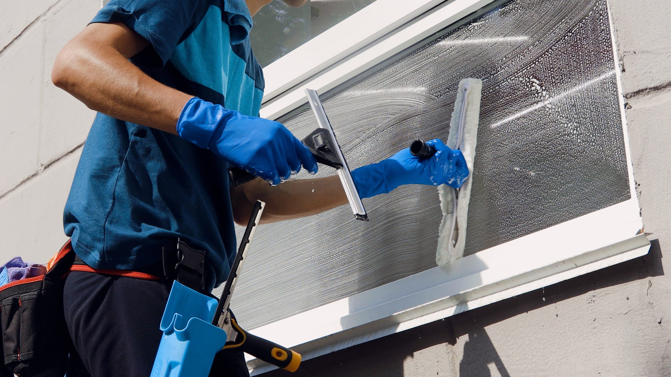 Male professional cleaning service worker in overalls cleans the windows and shop windows of a store with special equipment.